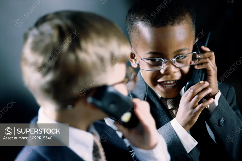 Two young boys dressed as businessmen talking on mobile phones