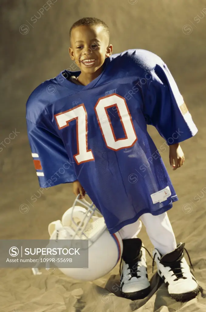 Boy in an oversized football uniform holding a helmet