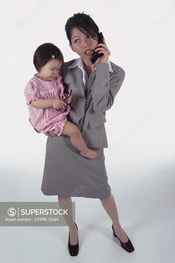 Portrait of a mother carrying her daughter talking on a mobile phone