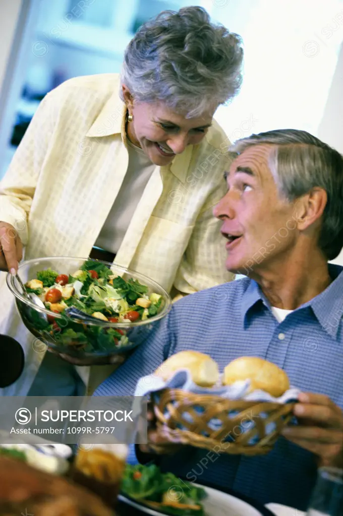 Senior woman holding a bowl of salad looking at a senior man