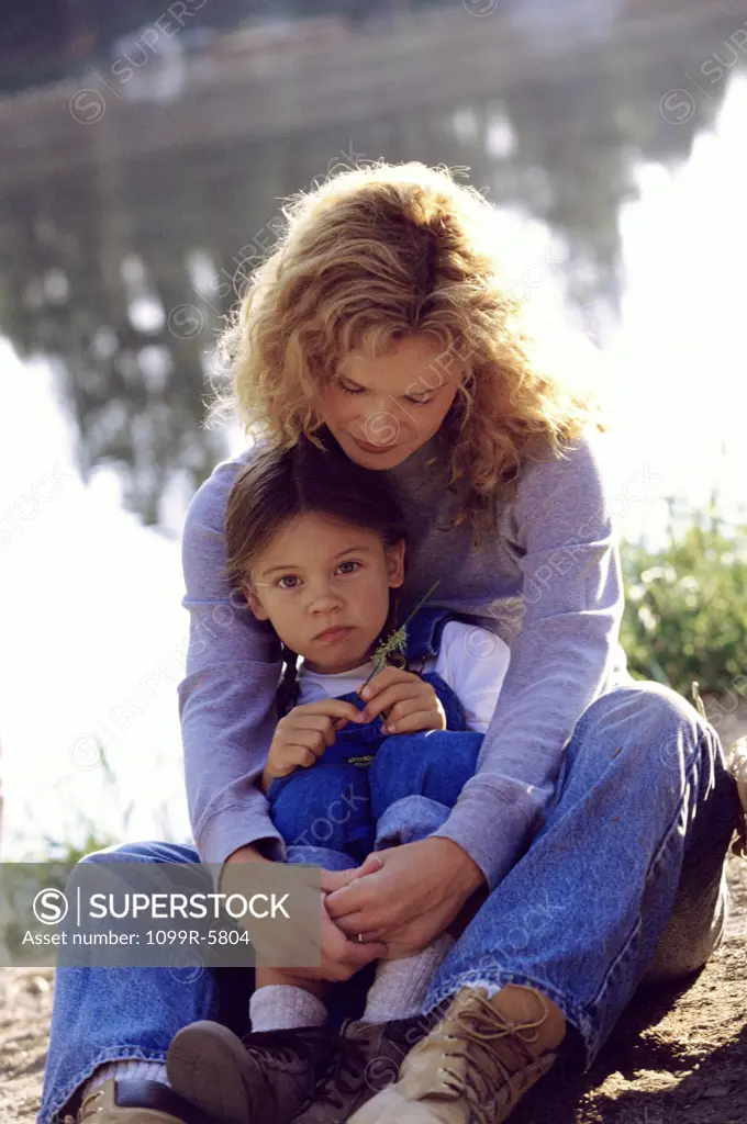 Young woman sitting with her daughter near a pond