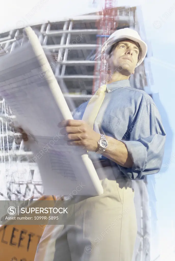 Engineer standing at a construction site holding blueprints