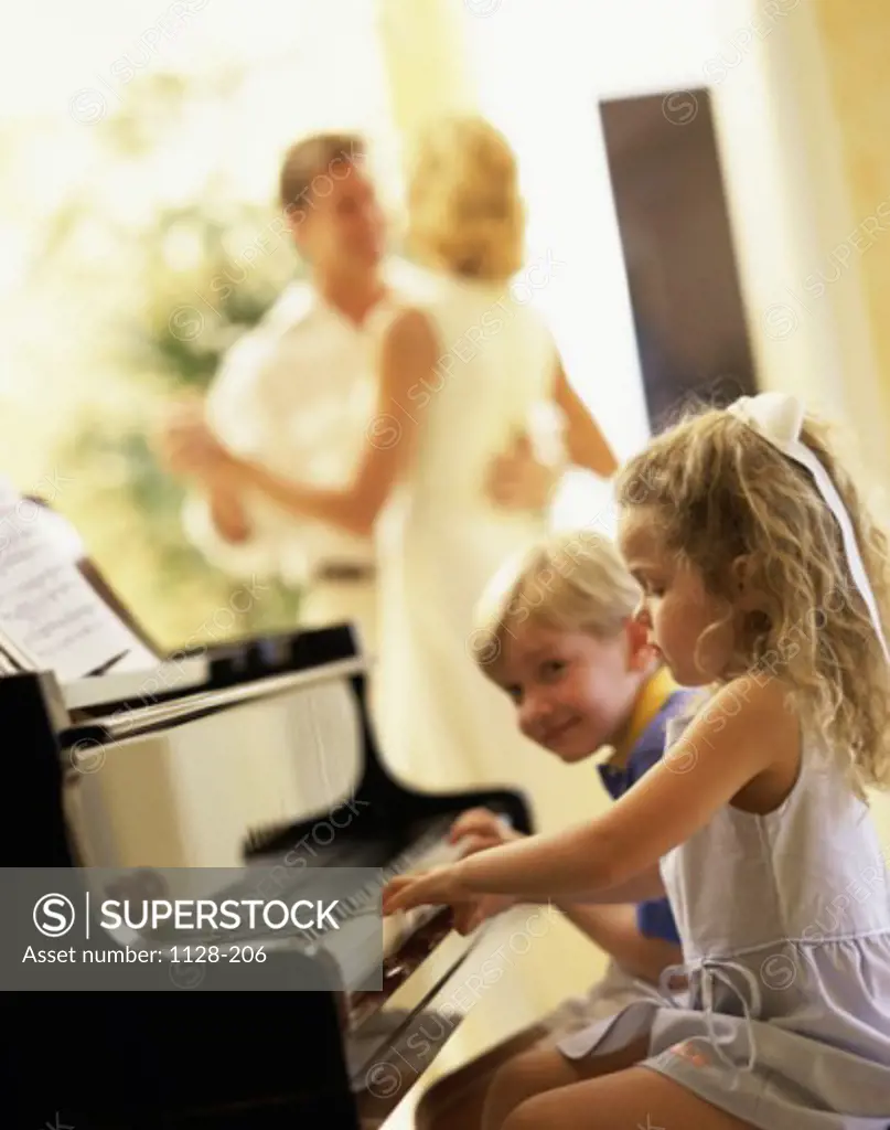 Side profile of children playing the piano with their parents dancing behind them