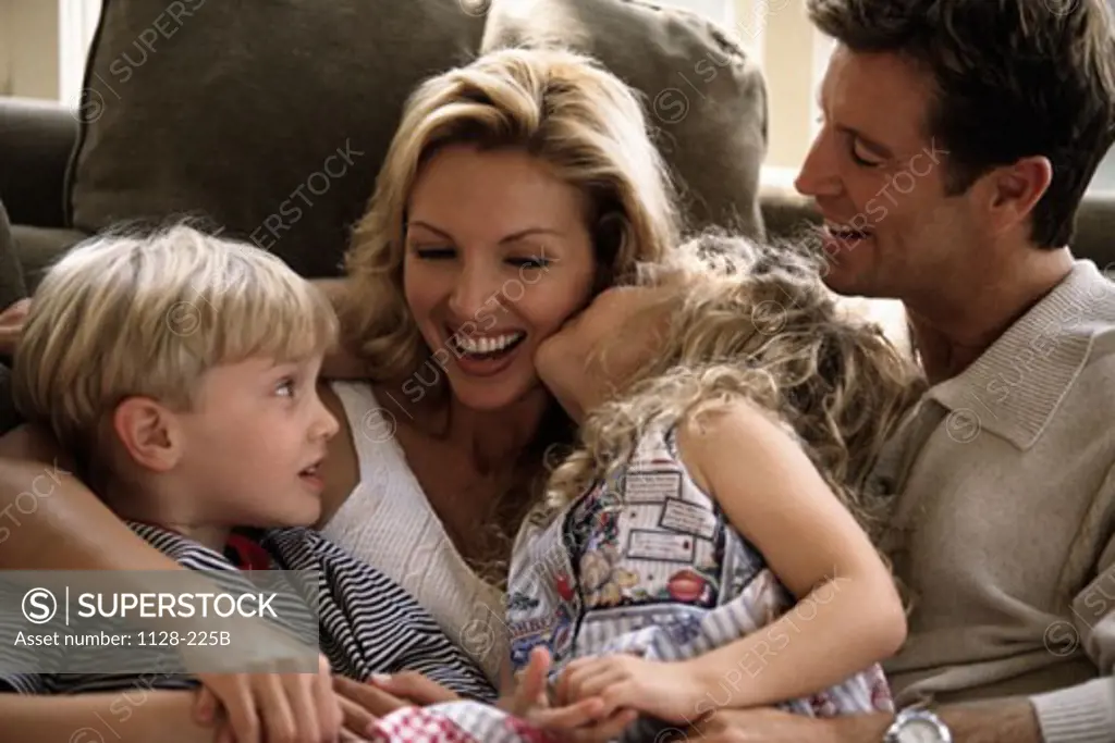 Close-up of a mid adult couple sitting on a couch with their son and daughter smiling