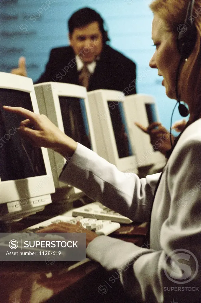 Businesswoman wearing a headset pointing to a computer monitor