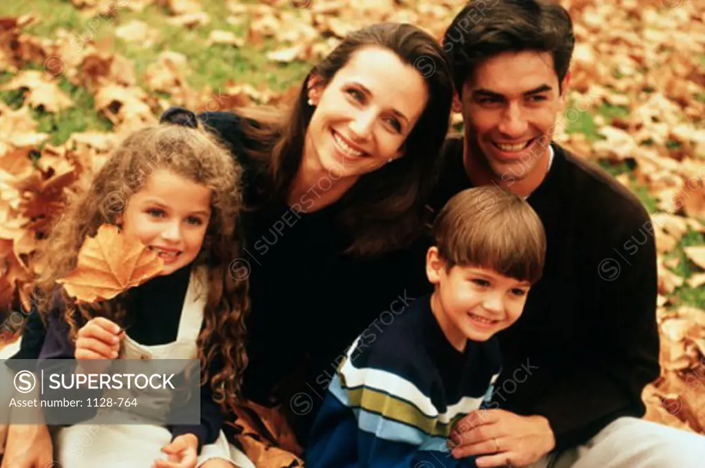 Close-up of a mid adult couple with their two sons and a daughter sitting in a park and smiling