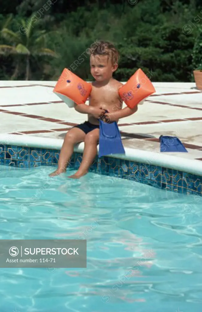 Boy sitting at the poolside with water wings on his arms