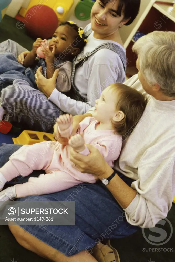 Baby boy and a baby girl sitting on a young woman and a mature woman's lap