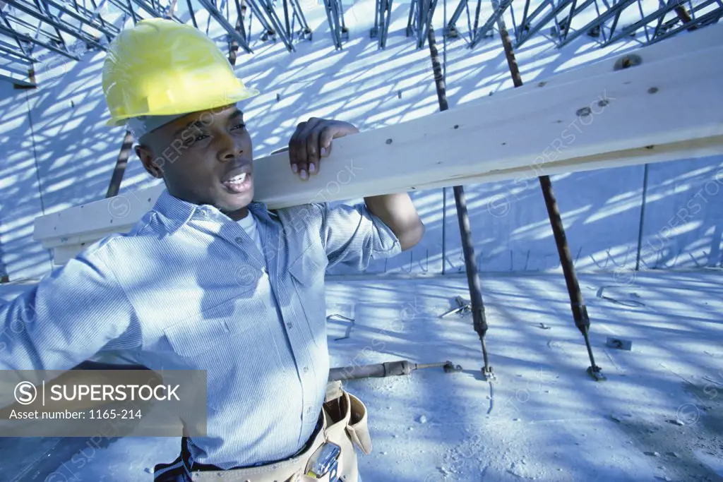 Young man carrying lumber on his shoulder at a construction site