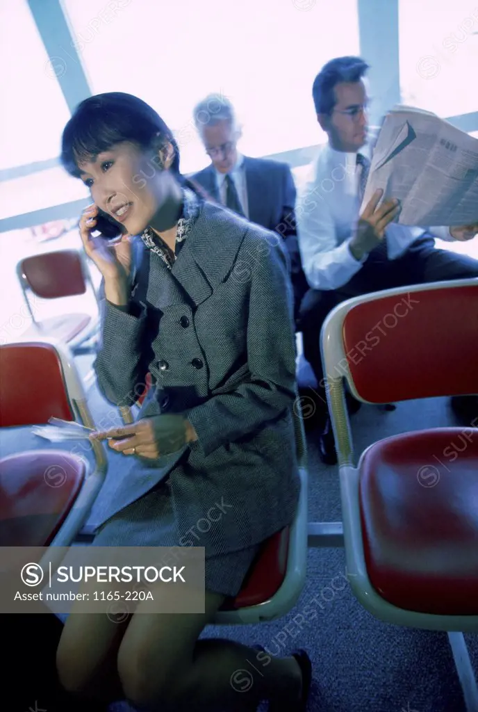 Businesswoman talking on a mobile phone sitting in front of two businessmen at an airport