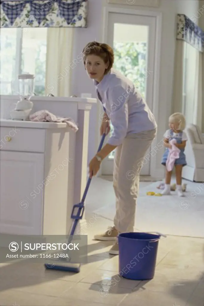 Portrait of a mother cleaning the floor with her daughter standing behind her