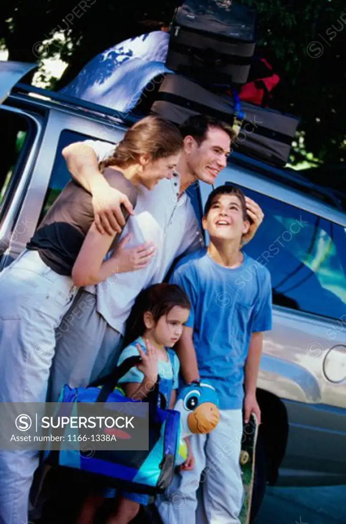 Parents and their two children standing with their luggage near a car