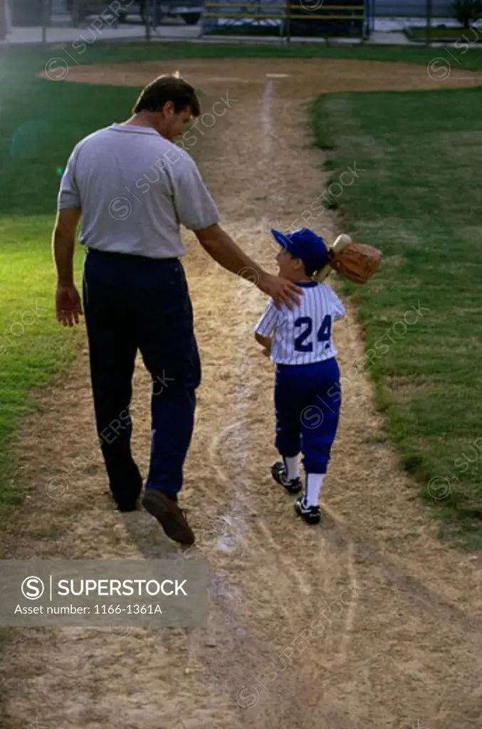Rear view of a man walking with his son at a playing field