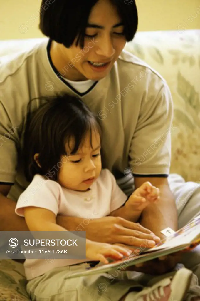 Teenage boy reading a book to a baby girl