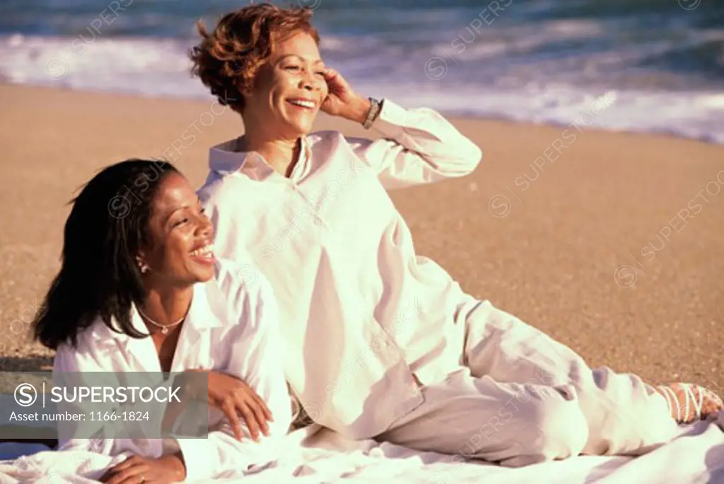 Mature woman lying with her adult daughter on the beach smiling