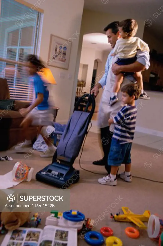 Father vacuuming a room with his two sons and a daughter