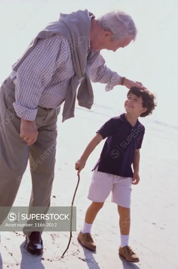 A child walking on the beach with his grandfather