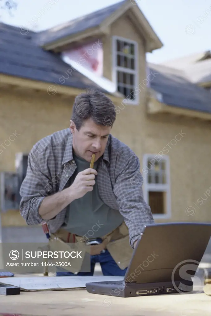 Mature man wearing a tool belt looking at a laptop
