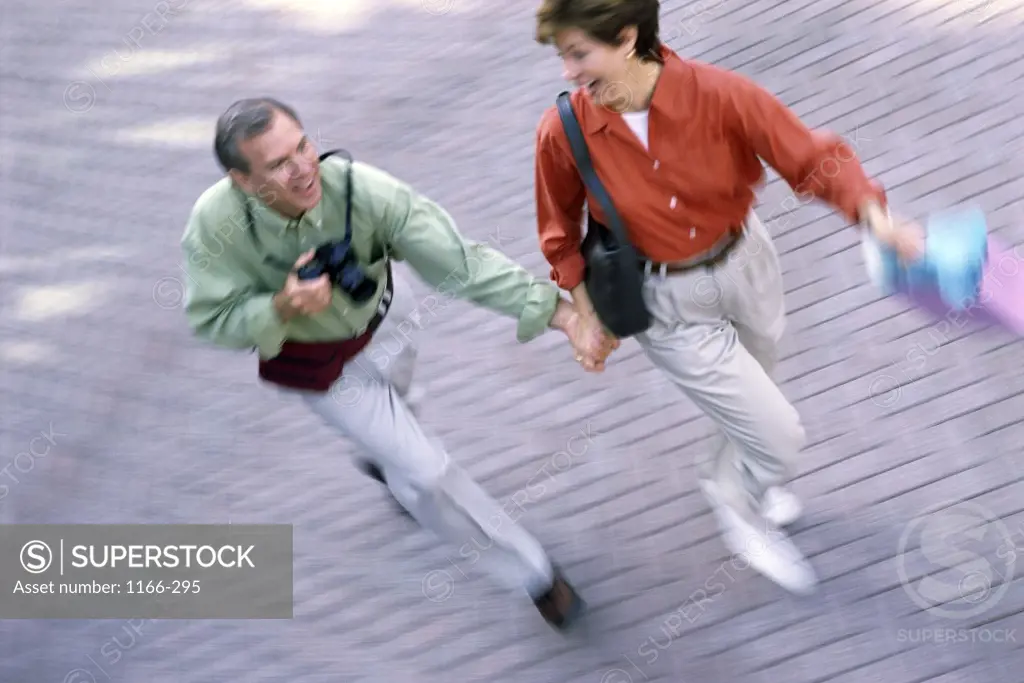 Mid adult couple running holding shopping bags and a camera