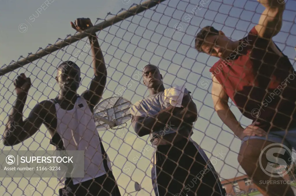 Portrait of three young men standing behind a chain-link fence