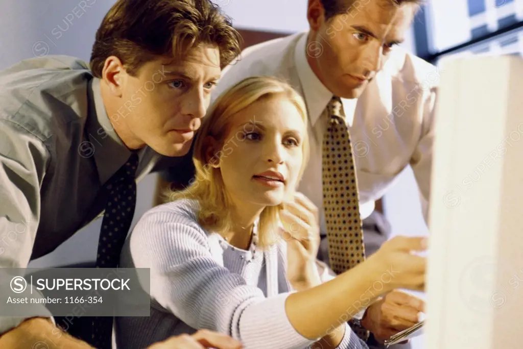 Two businessmen and a businesswoman in front of a computer monitor