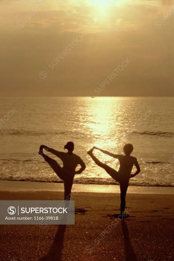 Silhouette of two people exercising on the beach