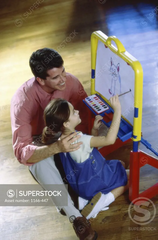 High angle view of a girl painting on an easel sitting beside her father
