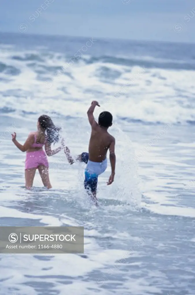 Rear view of a girl and a boy playing in the water on the beach