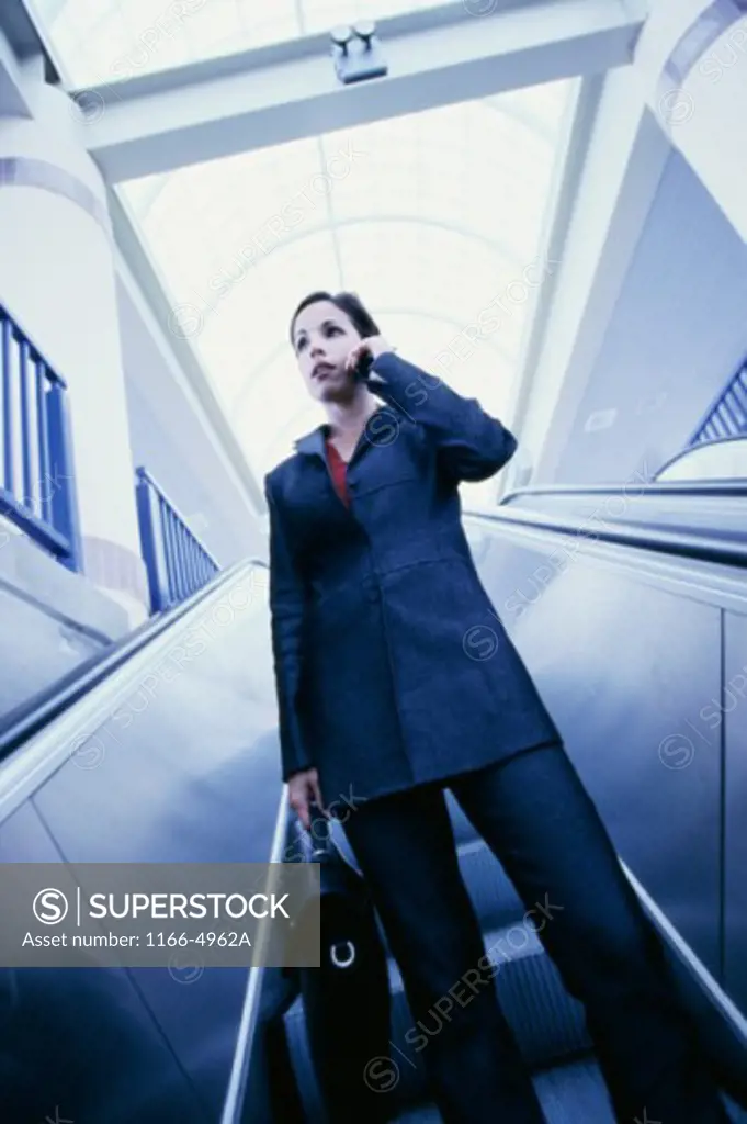 Low angle view of a businesswoman standing on an escalator talking on a mobile phone