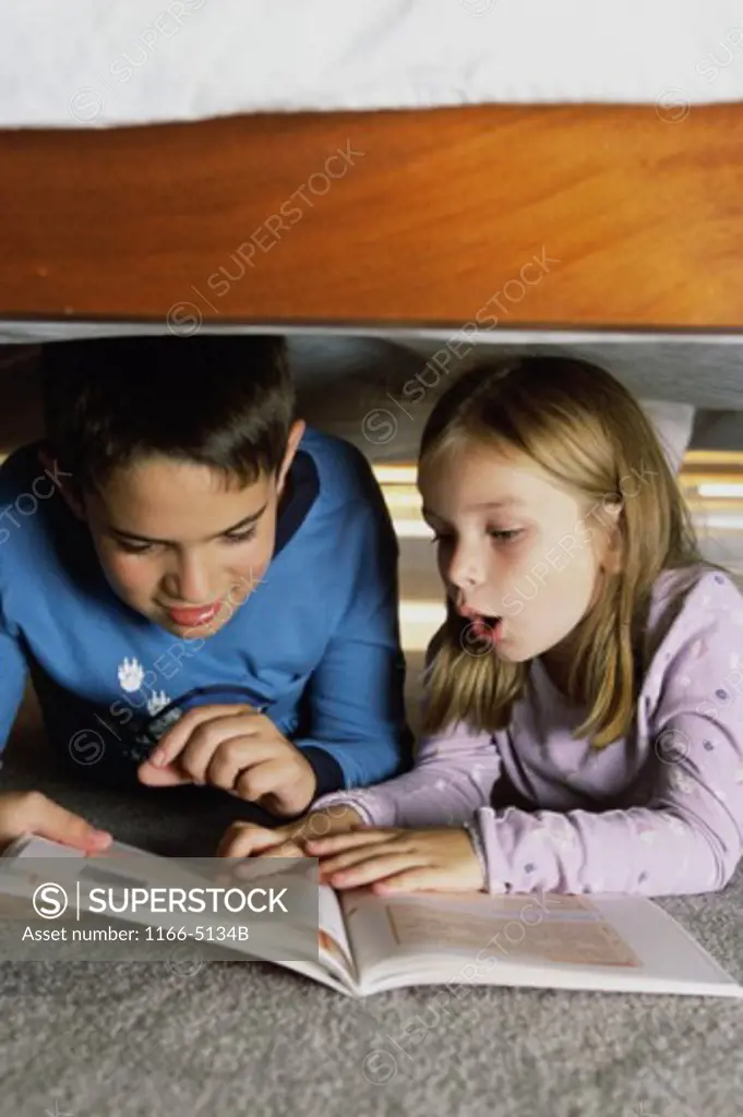 Boy and a girl reading a book under the bed