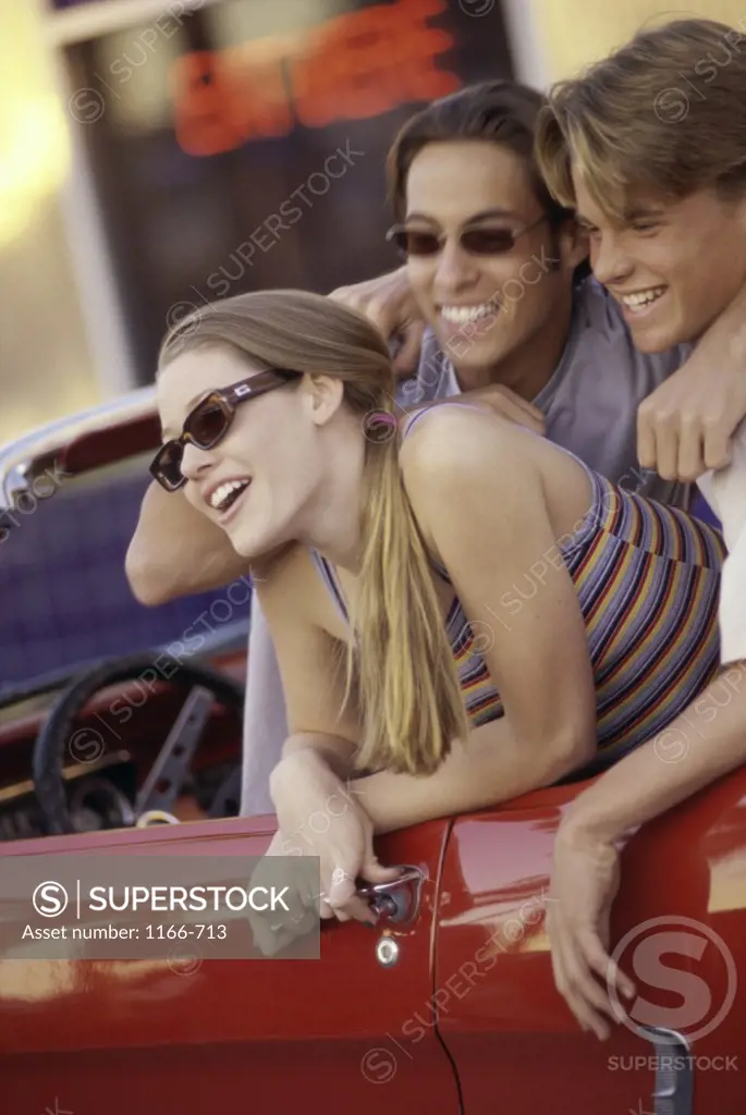Portrait of two teenage boys and a teenage girl sitting in a convertible car