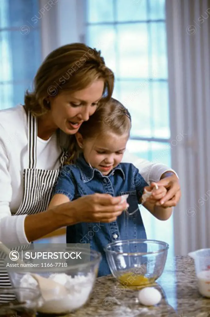 Mid adult woman with her daughter breaking eggs into a bowl