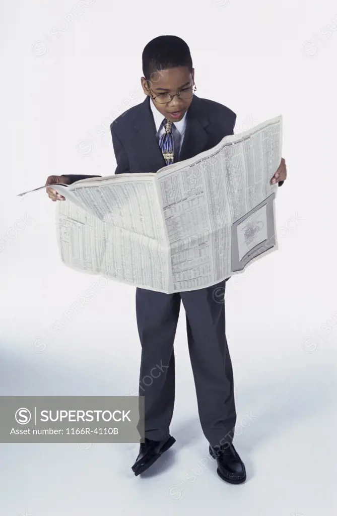 Portrait of a young boy dressed as a businessman reading a newspaper