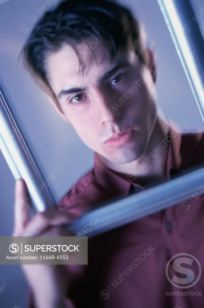 Portrait of a young man looking through a picture frame