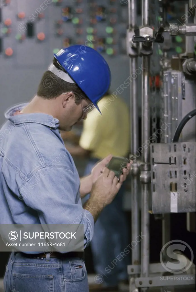 Worker standing beside machinery at a power plant operating a hand held device