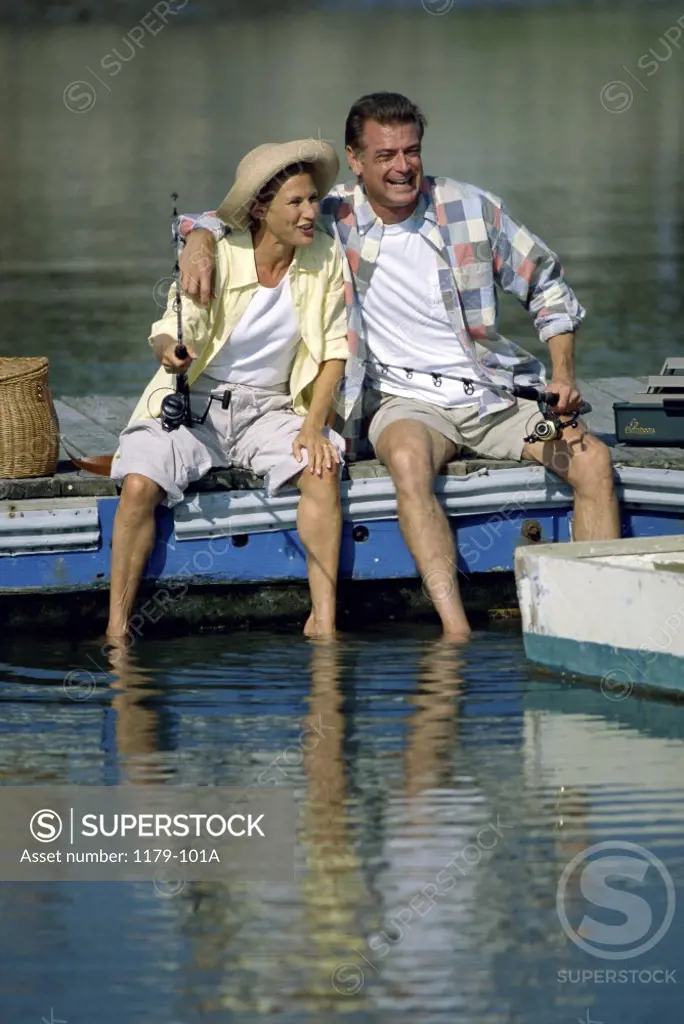 Mid adult couple sitting on a pier holding fishing rods