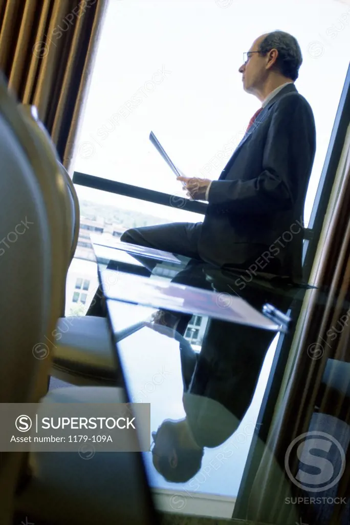 Side profile of a businessman holding a document looking through a window