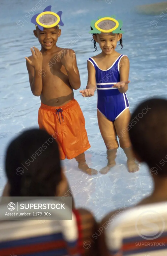 Boy and a girl standing in a swimming pool in front of their parents