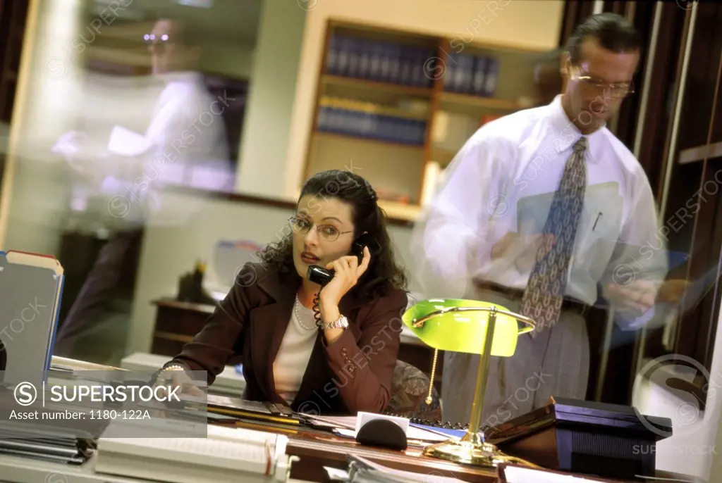 Businesswoman talking on the telephone with a businessman standing beside her