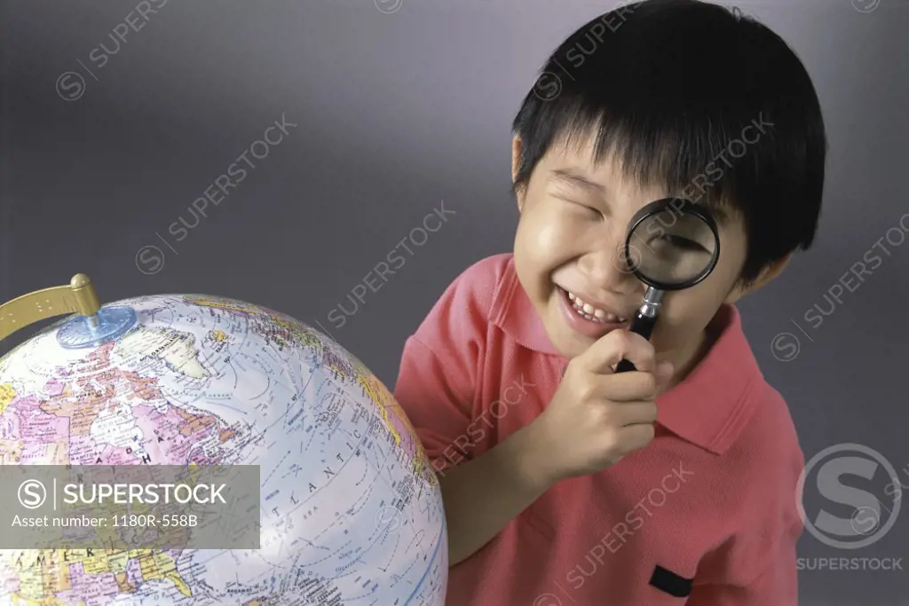 Portrait of a boy looking through a magnifying glass near a globe