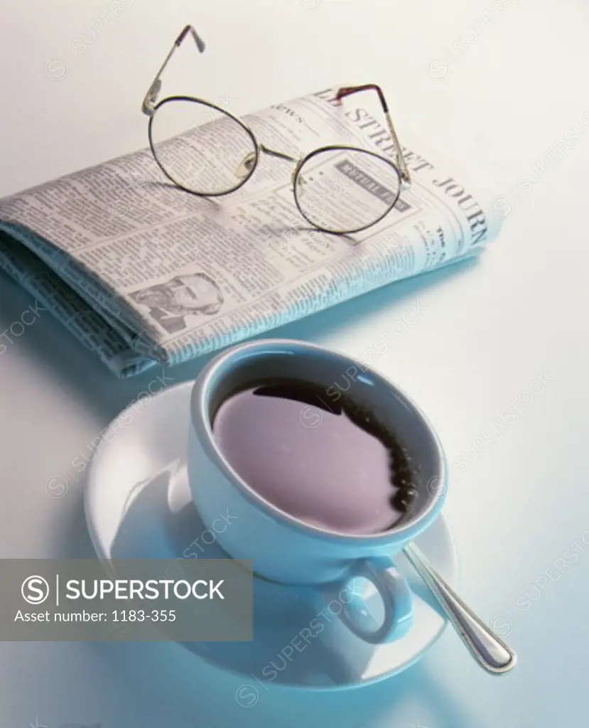 Close-up of a cup of black coffee with a financial newspaper and eyeglasses
