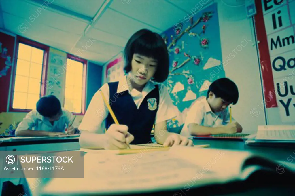 Low angle view of a girl writing with a pencil in a classroom