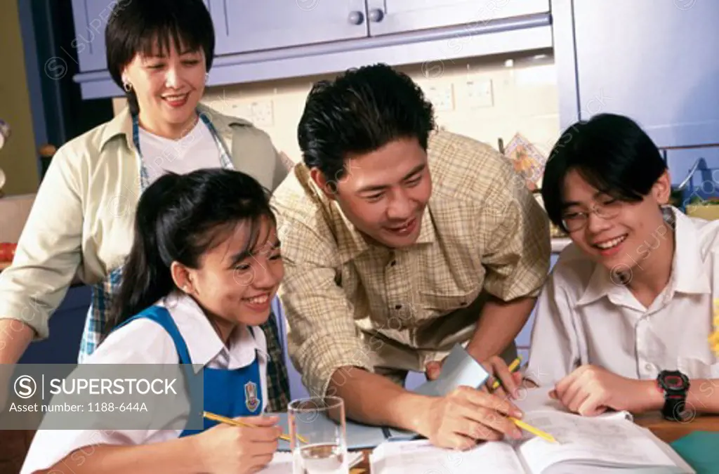 Close-up of a mid adult man helping his daughter and son with their homework with a mid adult woman standing beside them
