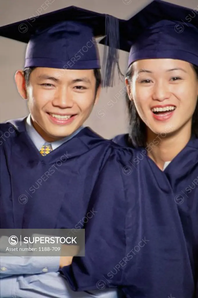 Portrait of a young man and a young woman wearing graduation gowns smiling