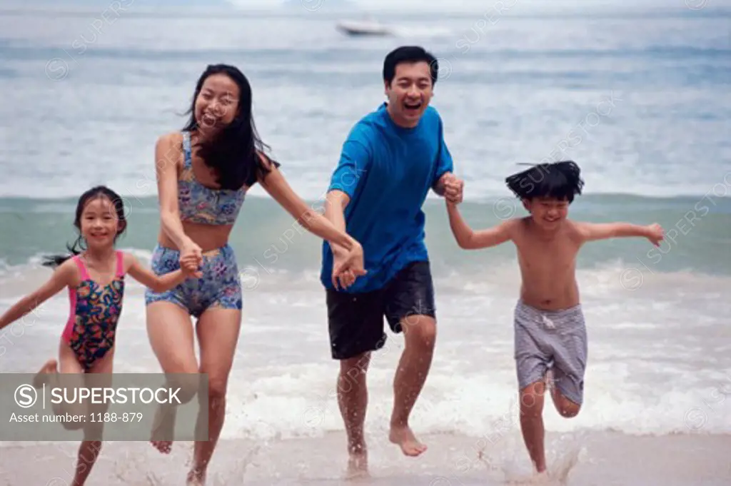 Mid adult couple with their son and daughter holding hands and running on the beach