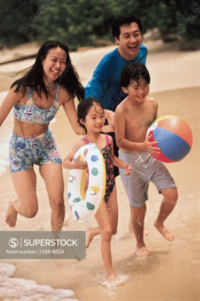 Mid adult couple with their son and daughter running on the beach
