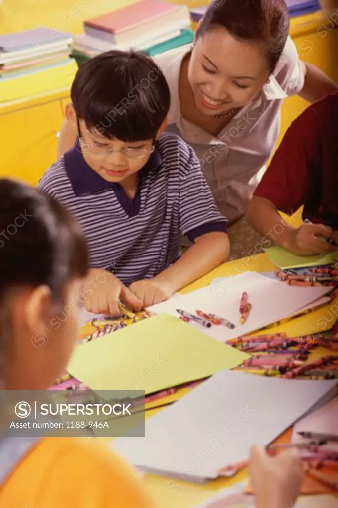 Boy drawing with crayons and a teacher looking at him