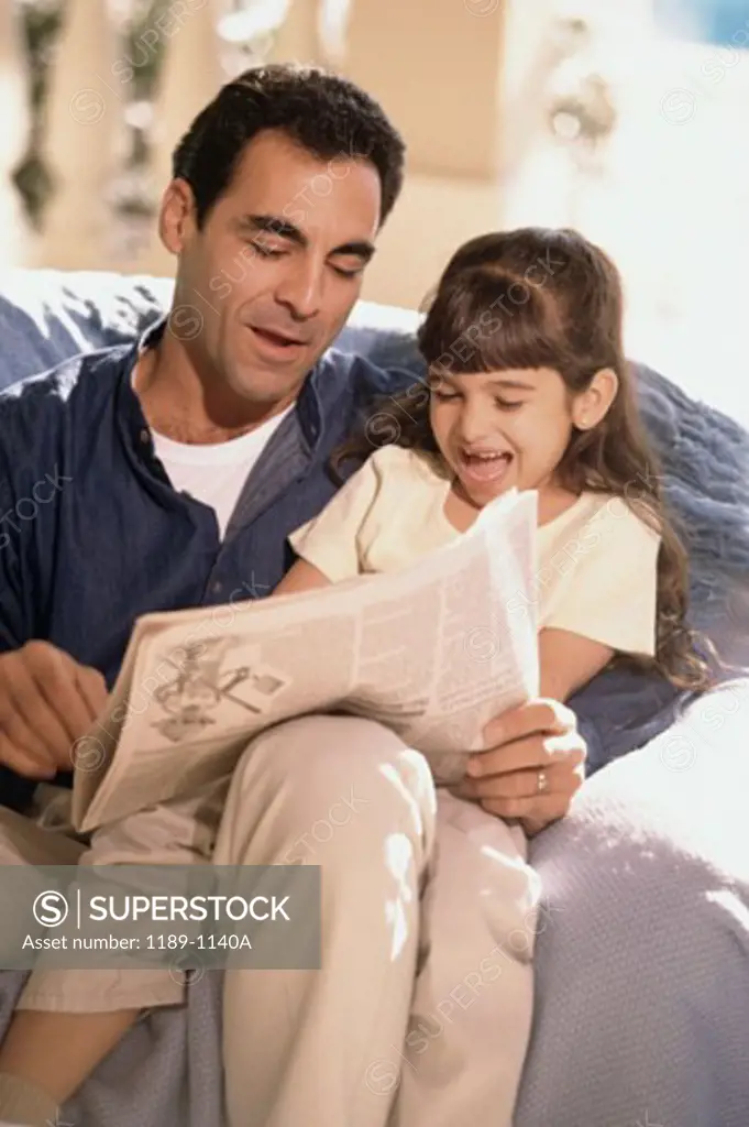 Close-up of a mid adult man with his daughter reading a newspaper