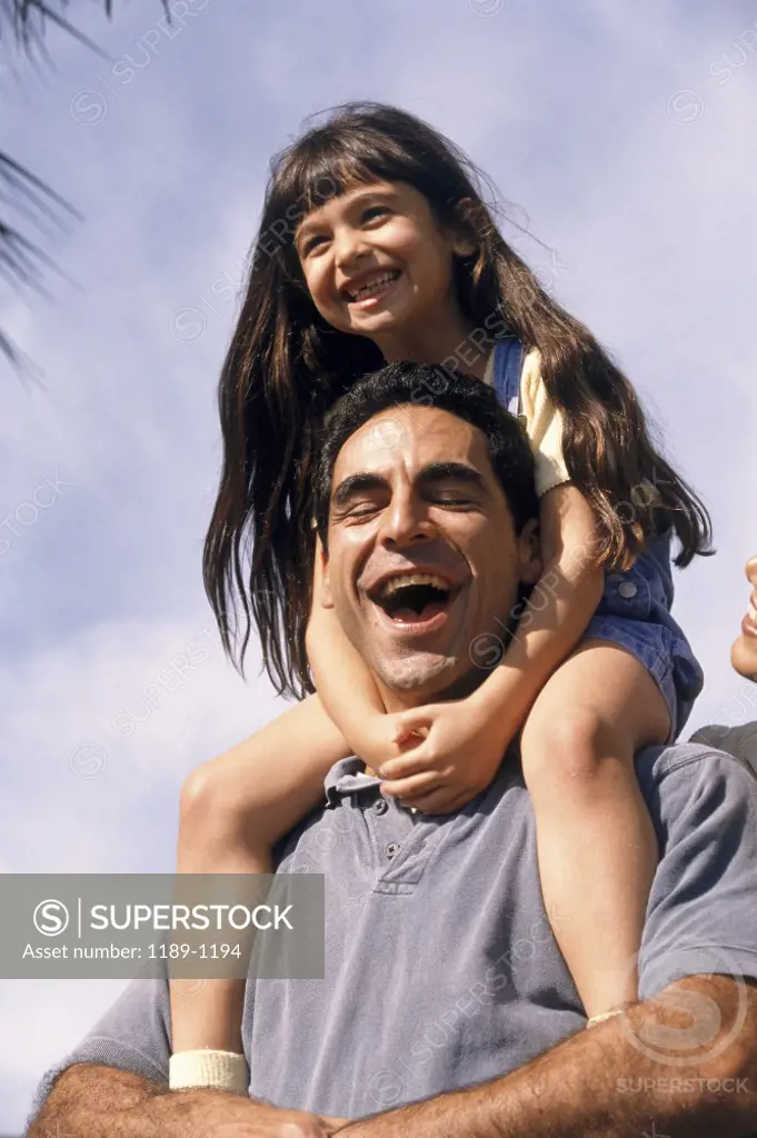 Low angle view of a mid adult man carrying his daughter on his shoulders