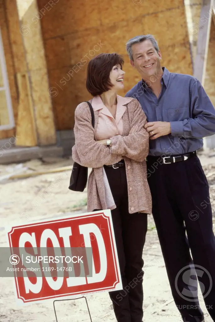 Mature couple standing in front of a house with a sold sign